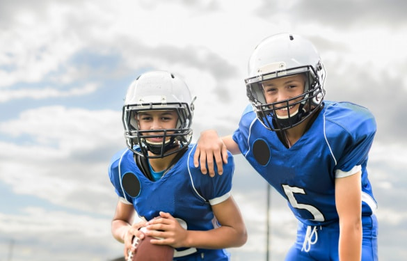 two young football players smile with a cloudy sky in the background